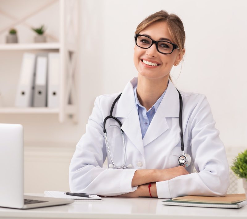 Lady Doctor Smiling At Camera Sitting In Modern Clinic Office